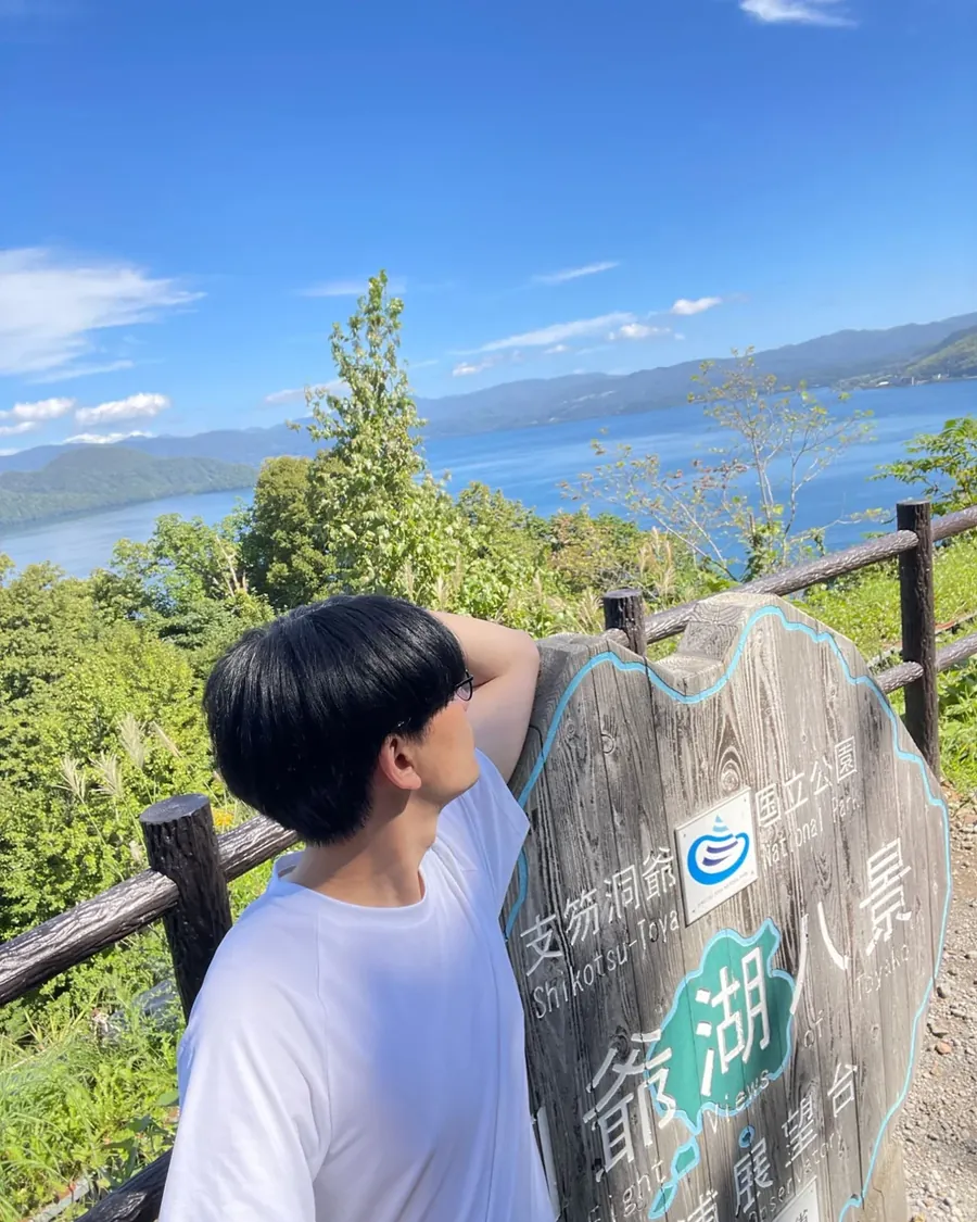 洞爺湖を見下ろす展望台で、「洞爺湖八景」の看板にもたれて湖を見る人。